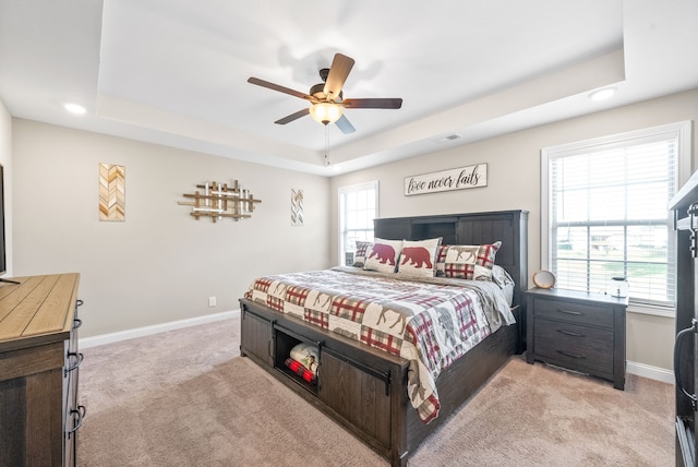 carpeted bedroom with ceiling fan and a tray ceiling