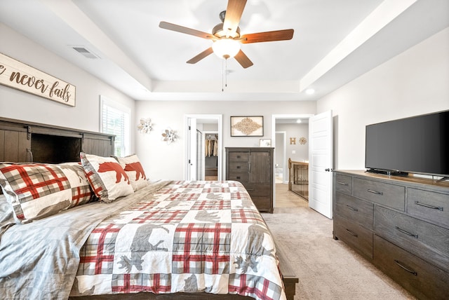 bedroom with light carpet, a closet, a tray ceiling, a spacious closet, and ceiling fan