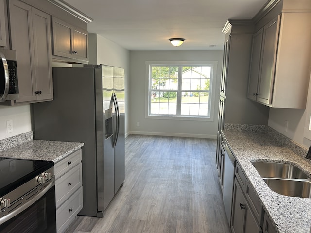 kitchen featuring light wood-type flooring, appliances with stainless steel finishes, light stone countertops, and gray cabinets