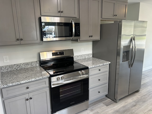 kitchen featuring stainless steel appliances, gray cabinetry, light stone countertops, and light hardwood / wood-style floors