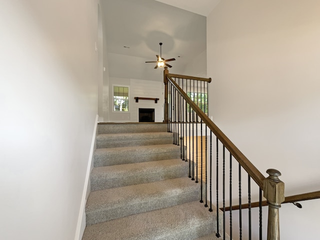 staircase with ceiling fan, a large fireplace, and carpet floors