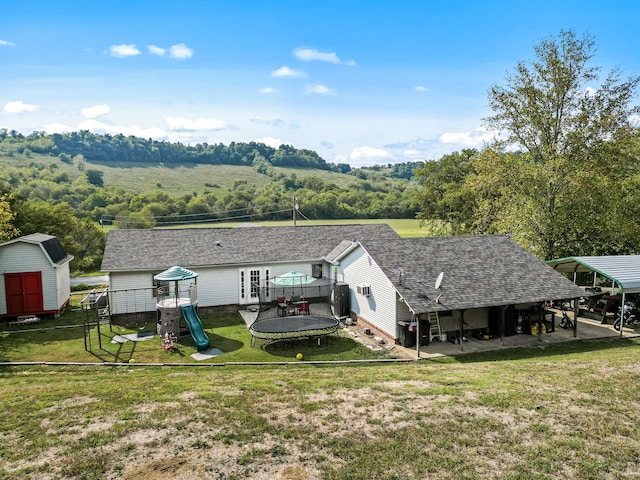 back of house featuring a playground, a yard, a storage shed, and a trampoline