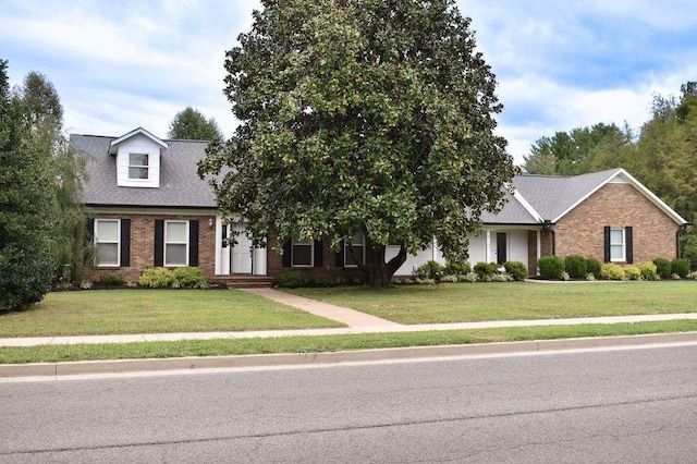 view of front of house featuring brick siding, roof with shingles, and a front lawn