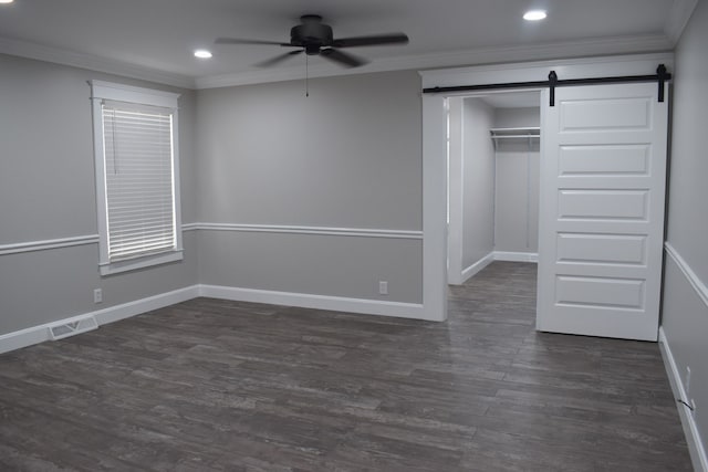 unfurnished bedroom featuring crown molding, dark hardwood / wood-style flooring, ceiling fan, and a barn door