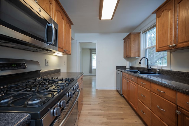 kitchen with appliances with stainless steel finishes, light hardwood / wood-style floors, dark stone counters, and sink