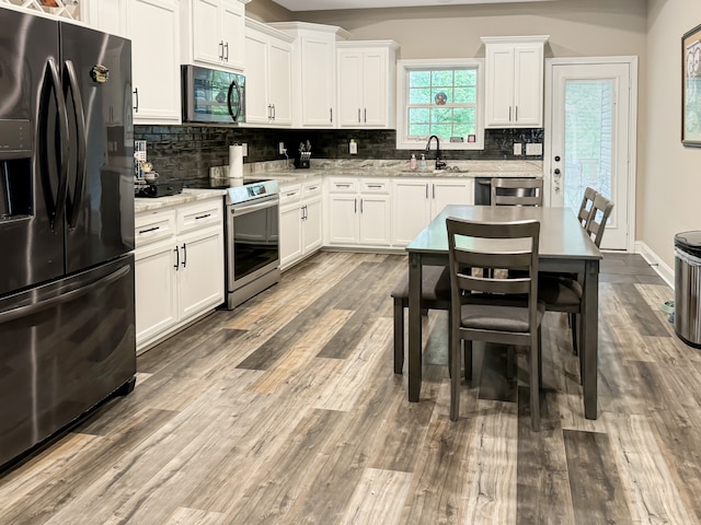 kitchen featuring stainless steel appliances, white cabinetry, sink, wood-type flooring, and decorative backsplash