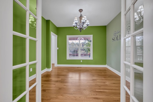 unfurnished dining area featuring french doors, wood-type flooring, and a chandelier