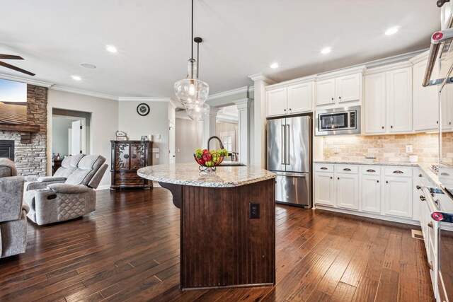 kitchen featuring a fireplace, appliances with stainless steel finishes, dark wood-type flooring, ceiling fan, and a center island with sink