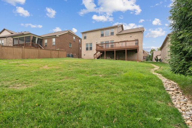 rear view of property featuring a wooden deck, a lawn, and a sunroom