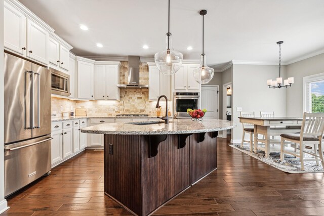 kitchen featuring a kitchen island with sink, dark wood-type flooring, stainless steel appliances, light stone counters, and wall chimney range hood