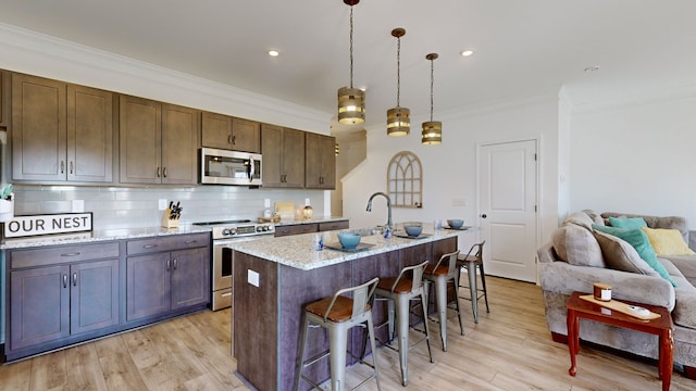 kitchen with light wood-type flooring, a center island with sink, appliances with stainless steel finishes, and decorative light fixtures