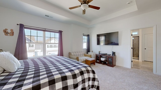 bedroom featuring light carpet, a tray ceiling, ceiling fan, and ensuite bathroom