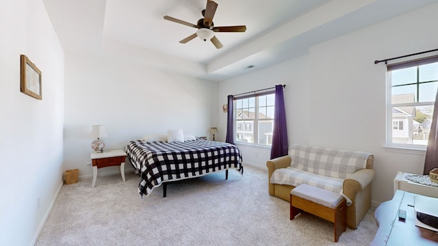 bedroom with light carpet, a tray ceiling, and ceiling fan