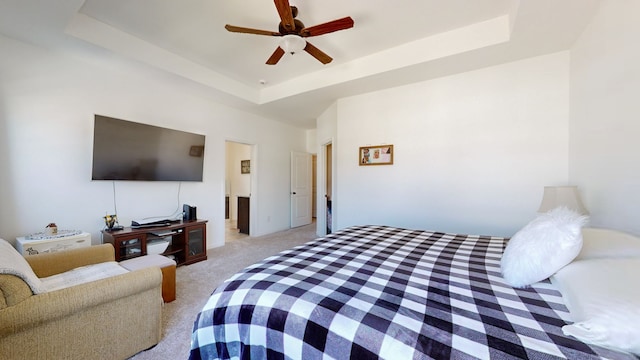 bedroom featuring a tray ceiling, light carpet, and ceiling fan