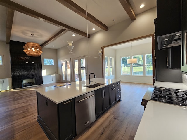 kitchen with a multi sided fireplace, an island with sink, sink, hanging light fixtures, and stainless steel dishwasher