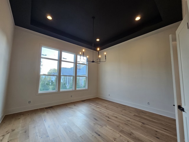 unfurnished room featuring an inviting chandelier, a tray ceiling, and light hardwood / wood-style floors