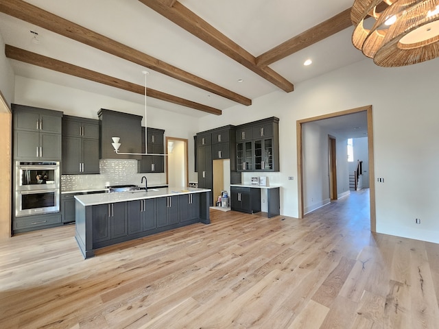 kitchen with a center island with sink, pendant lighting, light hardwood / wood-style flooring, appliances with stainless steel finishes, and beam ceiling