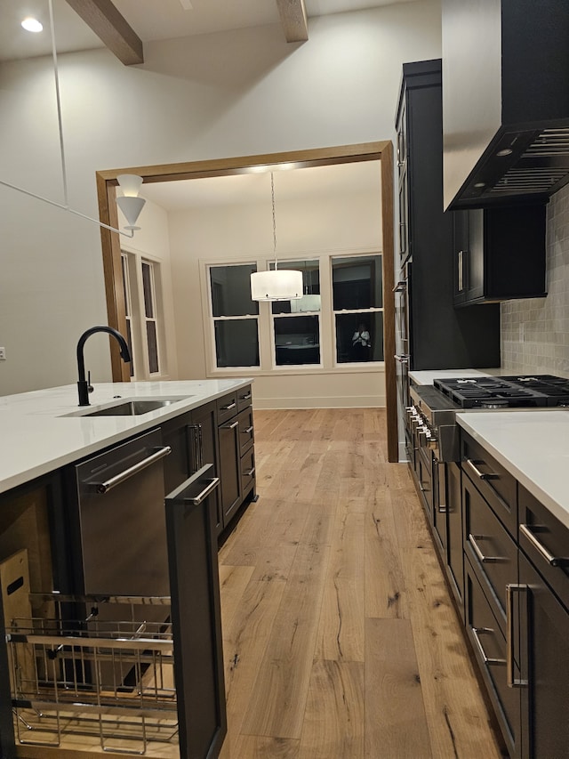 kitchen featuring range hood, backsplash, decorative light fixtures, light wood-type flooring, and sink