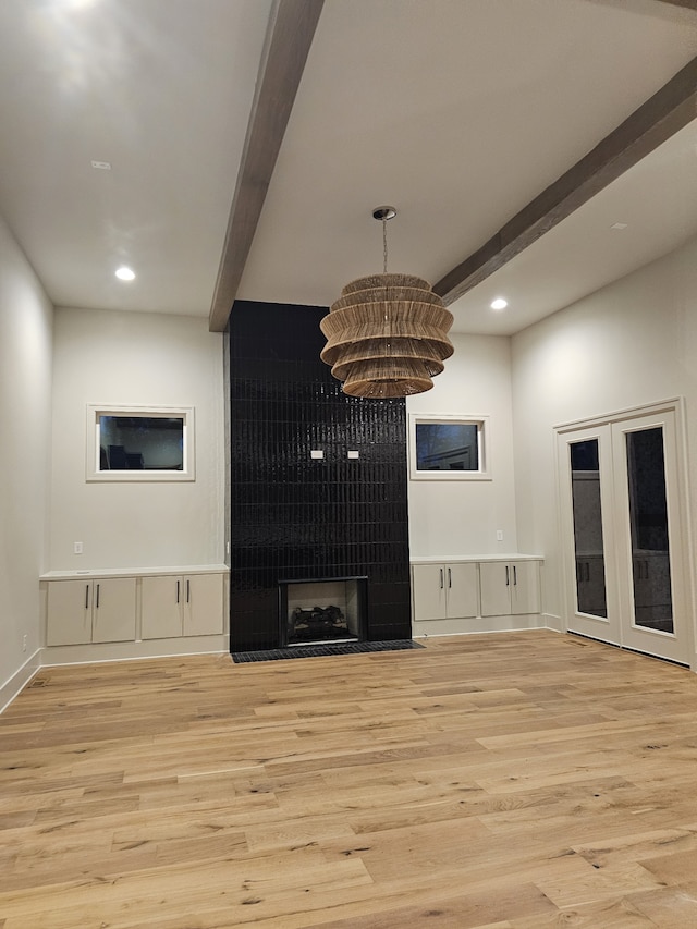 unfurnished living room featuring a tiled fireplace, an inviting chandelier, beamed ceiling, and light hardwood / wood-style flooring