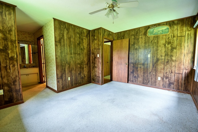 bedroom with light colored carpet, ensuite bath, wood walls, and ceiling fan