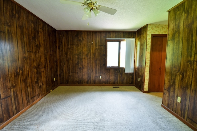 carpeted spare room with a textured ceiling, ceiling fan, and wood walls