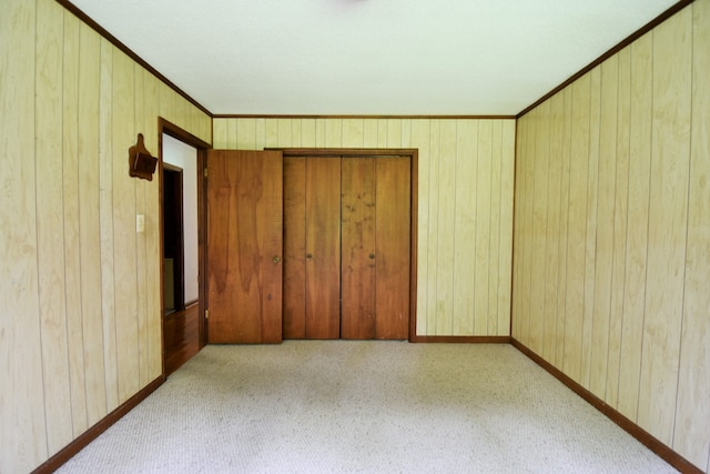 unfurnished bedroom with ornamental molding, wood walls, light colored carpet, and a closet