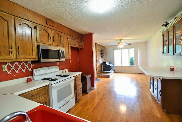 kitchen featuring a textured ceiling, a wood stove, white range with electric cooktop, ceiling fan, and light wood-type flooring