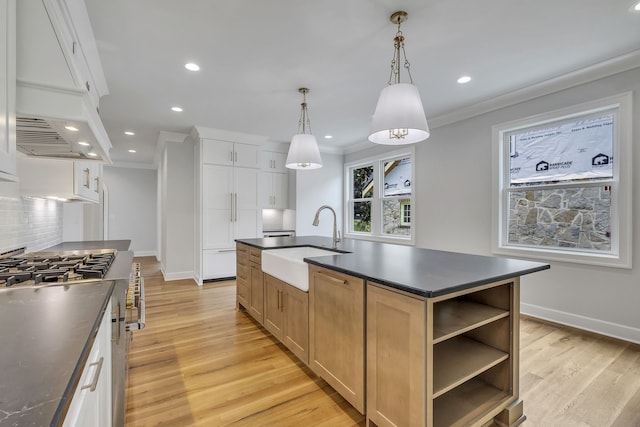 kitchen featuring high end range, sink, an island with sink, hanging light fixtures, and white cabinets