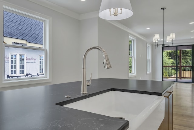 kitchen with pendant lighting, crown molding, wood-type flooring, an inviting chandelier, and sink