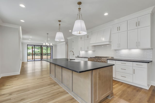 kitchen featuring light wood-type flooring, a large island with sink, white cabinetry, decorative light fixtures, and custom range hood