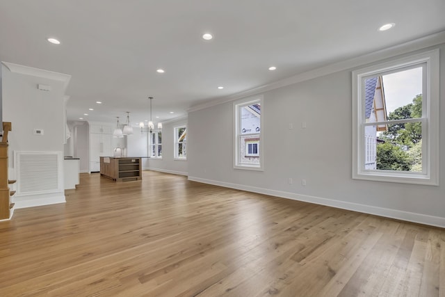 unfurnished living room featuring ornamental molding, an inviting chandelier, sink, and light hardwood / wood-style floors