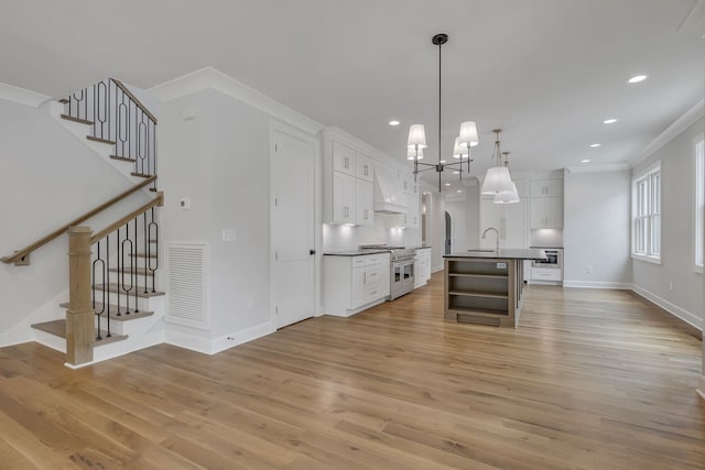 kitchen featuring ornamental molding, an island with sink, white cabinets, and light hardwood / wood-style floors