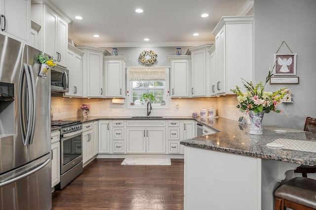 kitchen featuring stainless steel appliances, sink, kitchen peninsula, dark wood-type flooring, and a kitchen bar