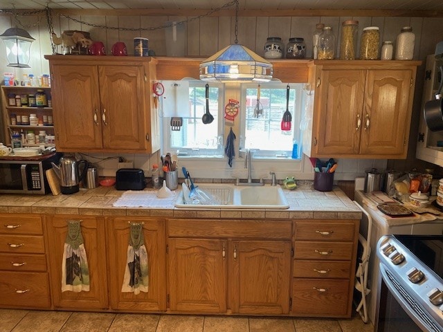 kitchen featuring white range oven, tile countertops, sink, and light tile patterned flooring