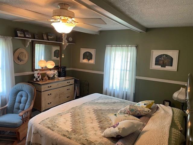 bedroom with beamed ceiling, ceiling fan, and a textured ceiling