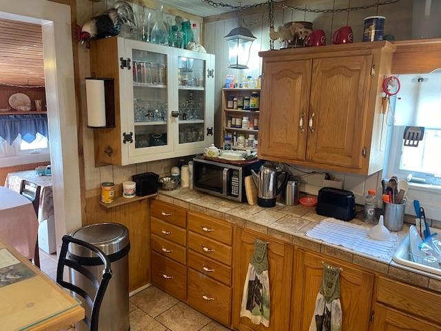 kitchen featuring tile countertops, stainless steel microwave, brown cabinetry, and light tile patterned floors