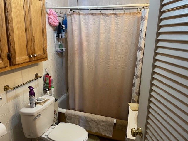 bathroom with tile walls, toilet, and shower / bathtub combination with curtain