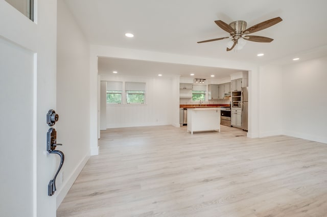 unfurnished living room featuring light wood-type flooring, ceiling fan, and sink