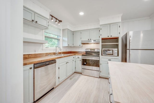 kitchen with butcher block countertops, light hardwood / wood-style flooring, appliances with stainless steel finishes, crown molding, and sink