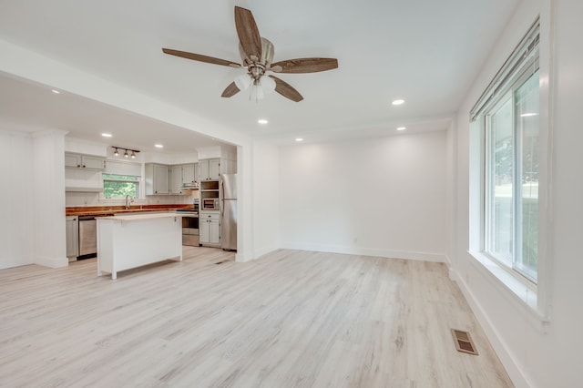 unfurnished living room with light wood-type flooring, ceiling fan, and sink