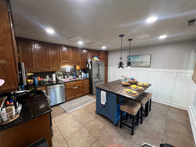 kitchen featuring a textured ceiling, a kitchen island, a kitchen breakfast bar, appliances with stainless steel finishes, and hanging light fixtures