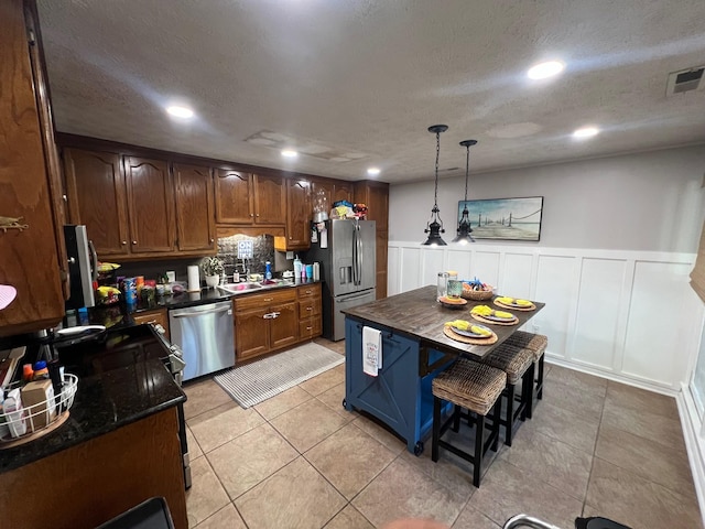 kitchen with visible vents, a sink, decorative light fixtures, a textured ceiling, and stainless steel appliances