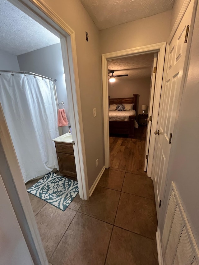 corridor with dark tile patterned flooring, baseboards, visible vents, and a textured ceiling