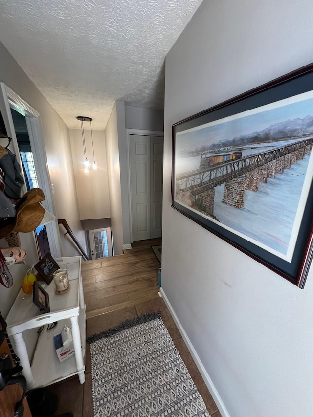 hall featuring an upstairs landing, baseboards, a textured ceiling, and wood finished floors