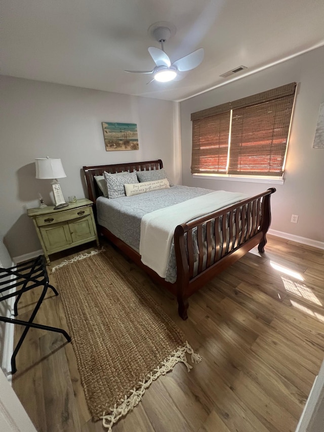 bedroom with ceiling fan, wood finished floors, visible vents, and baseboards