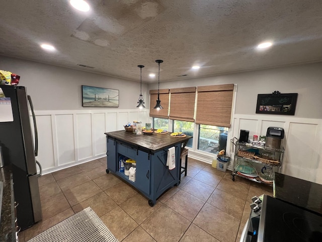 kitchen featuring blue cabinetry, freestanding refrigerator, a textured ceiling, wood counters, and a decorative wall