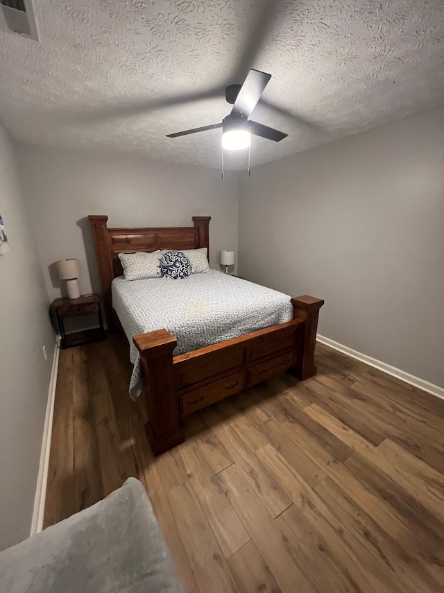 bedroom with a textured ceiling, wood-type flooring, and ceiling fan