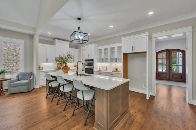 kitchen with a kitchen island with sink, dark wood-type flooring, white cabinets, and double oven