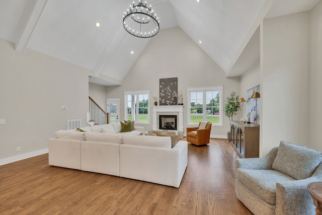 living room featuring a premium fireplace, light wood-type flooring, high vaulted ceiling, and an inviting chandelier