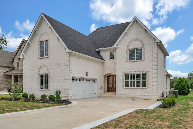 french country style house featuring central air condition unit, a garage, and a front lawn